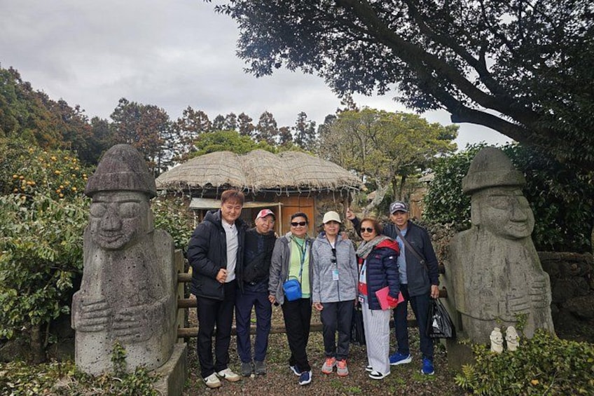 A group of people standing in front of stone statues and a traditional hut. 2