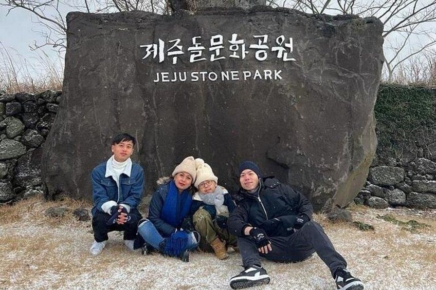 A group of people sitting in front of a large stone with text indicating it is Jeju Stone Park. 5