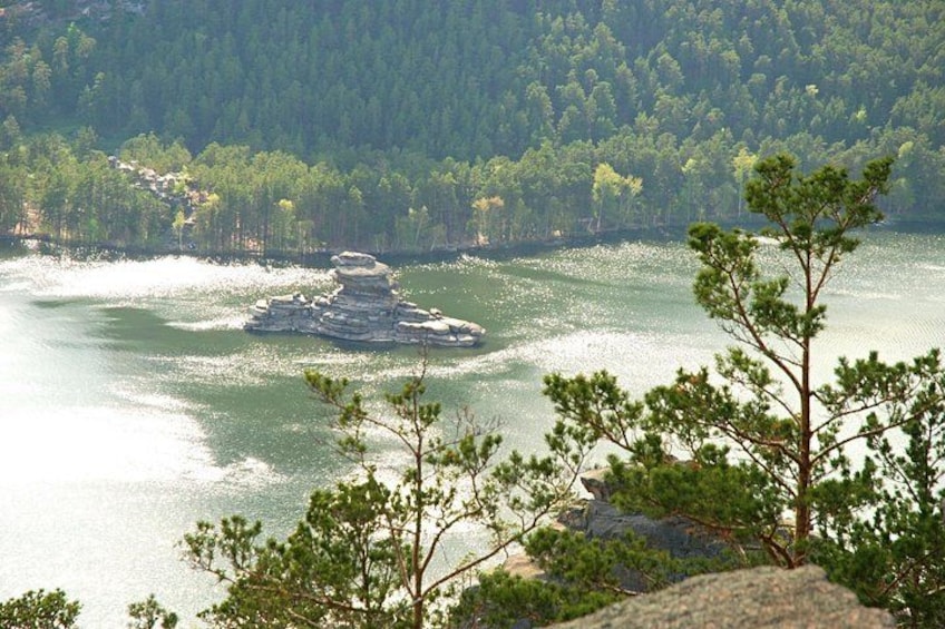 Ein See, umgeben von dichtem Wald, mit einer felsigen Landzunge in der Mitte. 4