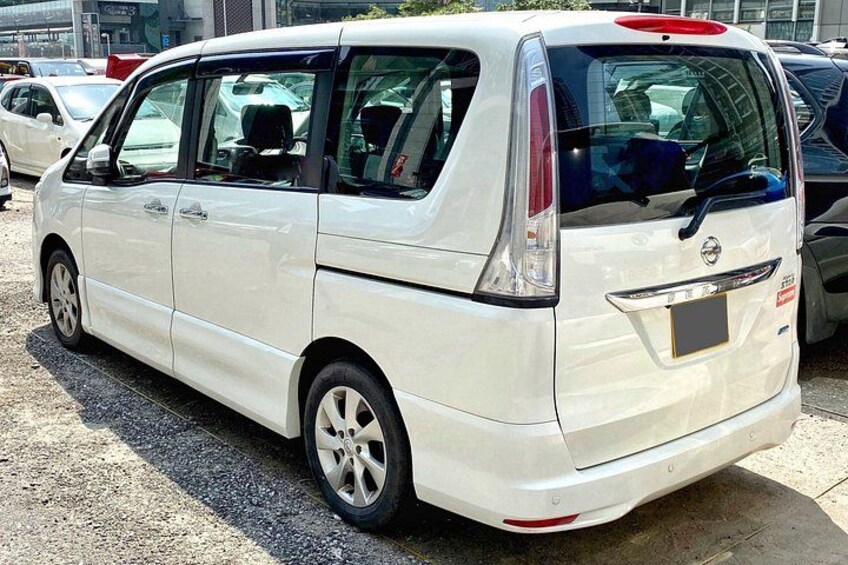 A white van parked on a gravel surface with visible side mirrors and a rear license plate. 4