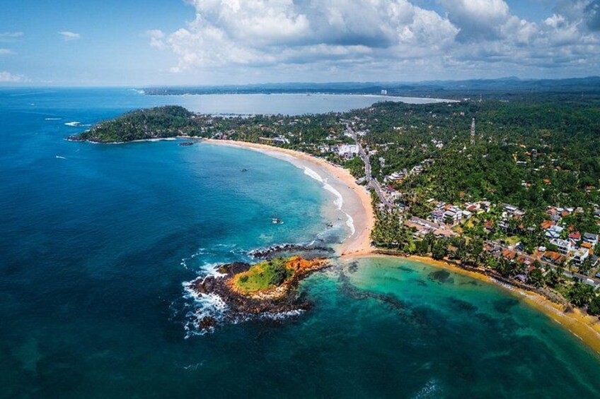 A coastal landscape with a beach, a small island, and a town. 2