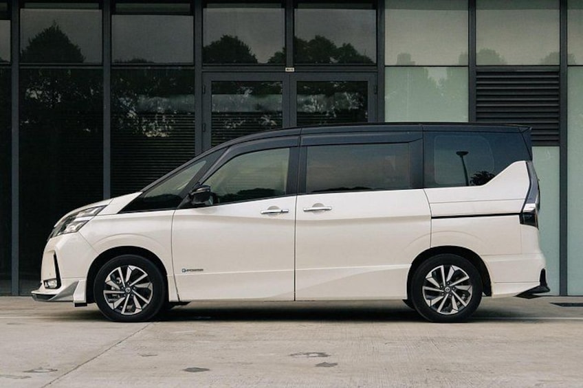 A white minivan parked in front of a building with large windows and a metal door. 1