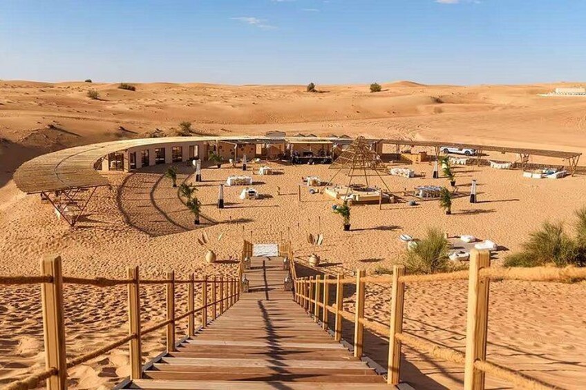 A desert resort with a wooden boardwalk leading to a building, surrounded by sand dunes. 2