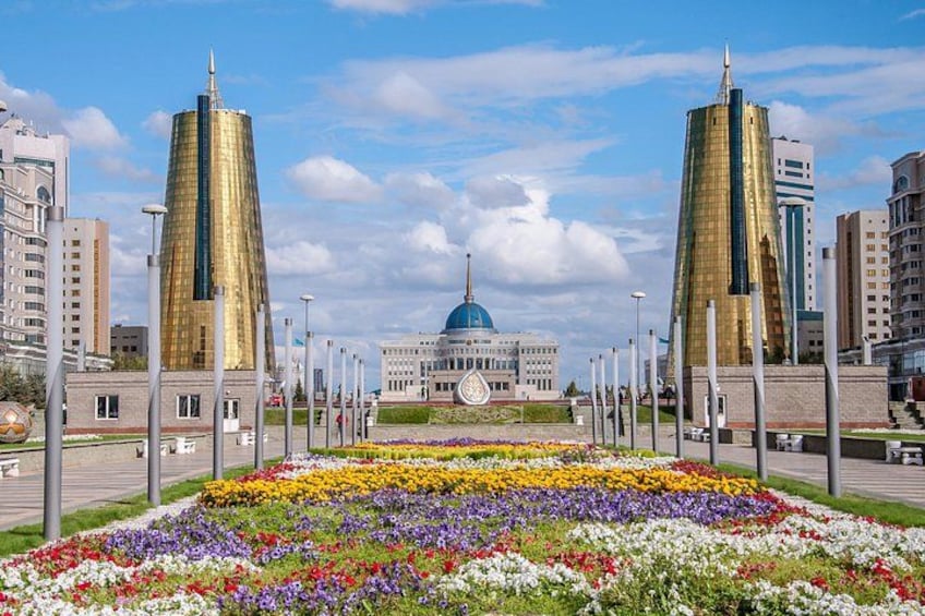 A city square with a central building, two tall structures, and a flower garden. 1