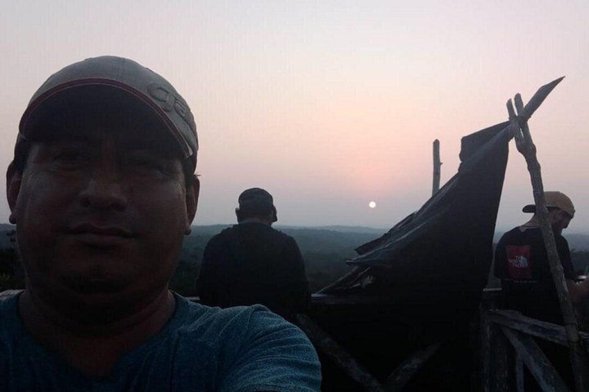A person in a blue shirt and cap, a wooden structure, and a sunset in the background. 2