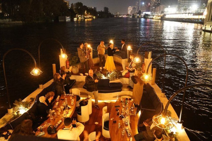 A boat with people dining and socializing, surrounded by water and city lights in the background. 5