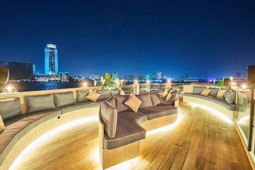 A rooftop lounge with a curved seating area, a city skyline in the background, and a wooden floor. 3