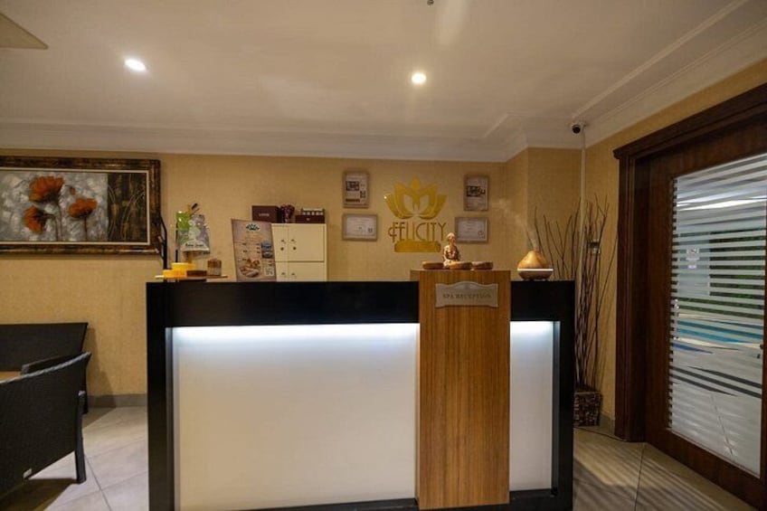 A reception desk with a wooden counter and a white panel, a framed picture on the wall, and a sign with a crown logo. 5