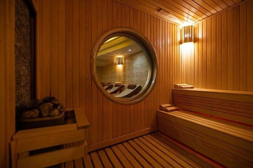 A wooden sauna with benches, a round mirror, and a stone wall. 3