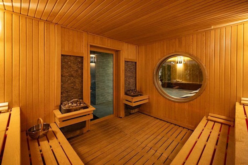 A wooden sauna with benches, a round mirror, and a wooden ceiling. 2