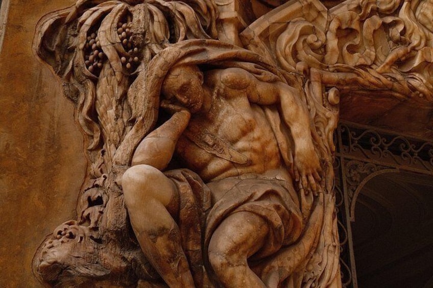Een gedetailleerde stenen sculptuur van een liggend figuur met een leeuwenkop, omringd door bladeren en begroeiing. 3