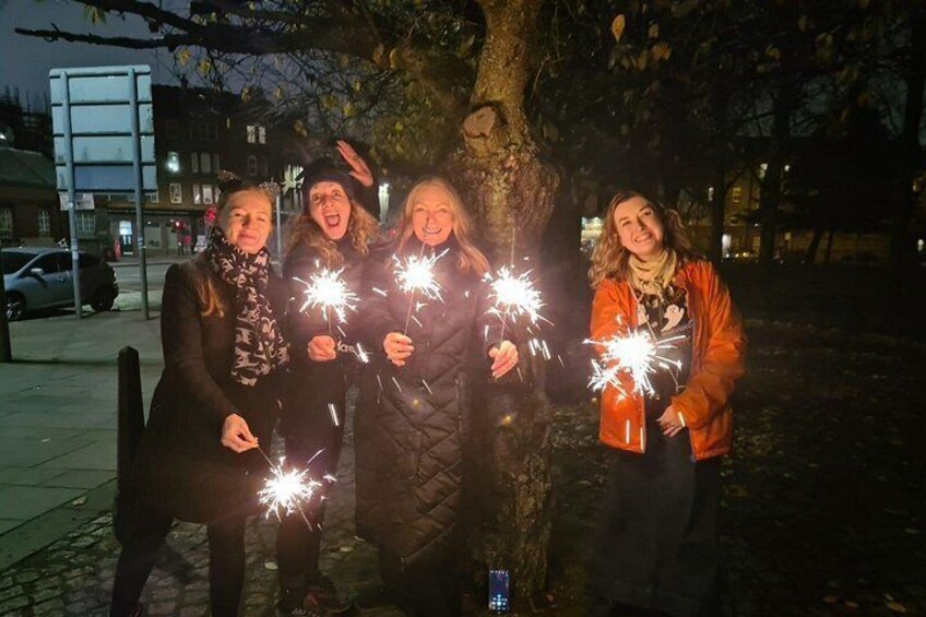 Four people holding sparklers, standing under a tree in a park at night. 3