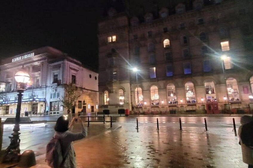 A nighttime urban scene with illuminated buildings and a wet plaza. 4