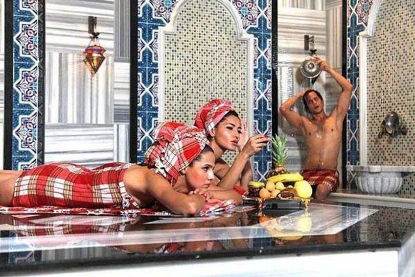 Una persona con un conjunto rojo y blanco a cuadros recostada sobre una superficie, otra persona vestida de rojo, y una tercera persona con shorts rojos de pie en una bañera. 2