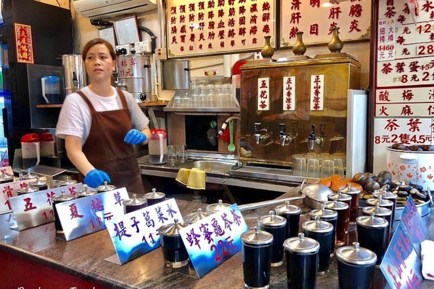 A person standing behind a counter with various containers and signs with text. 2