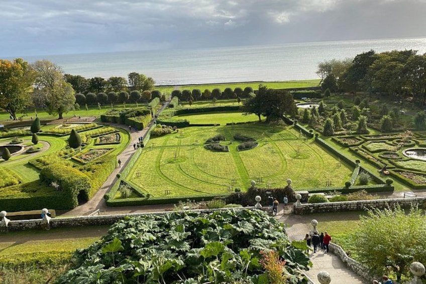 Een verzorgde tuin met geometrische paden, diverse bomen en uitzicht op zee. 4