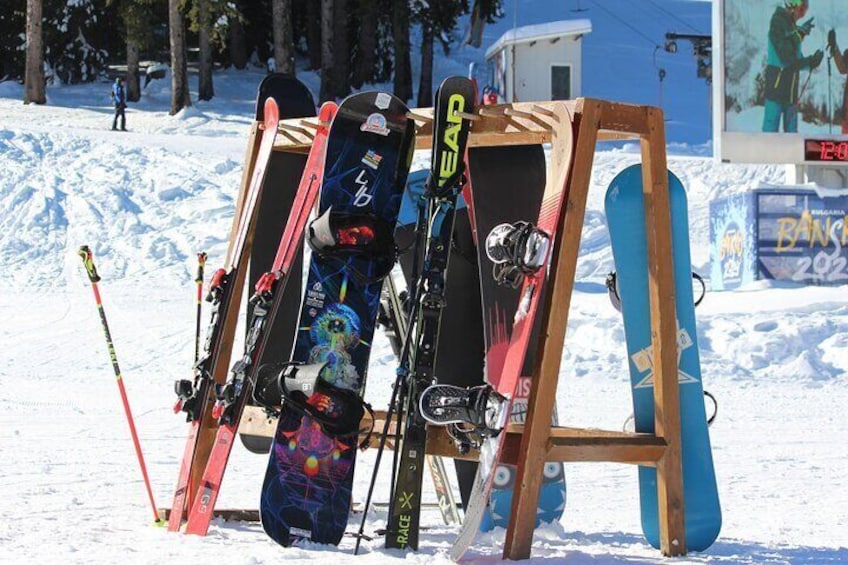 Skis and snowboards leaning against a wooden rack in a snowy area. 4