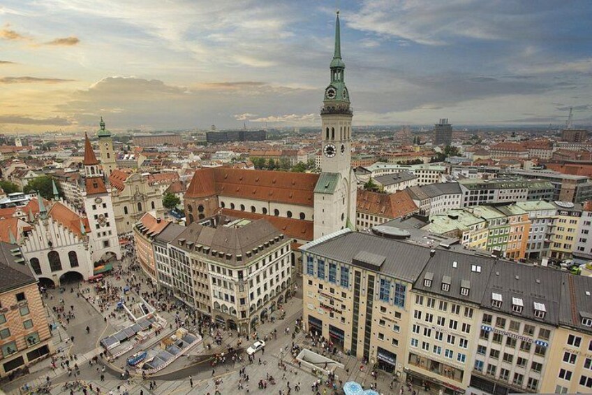 En stadsbild med historiska byggnader, ett framträdande kyrktorn och ett livligt torg. 4