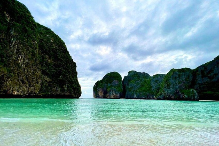Un paysage côtier caractérisé par une eau turquoise et limpide, des falaises rocheuses et un ciel nuageux. 3