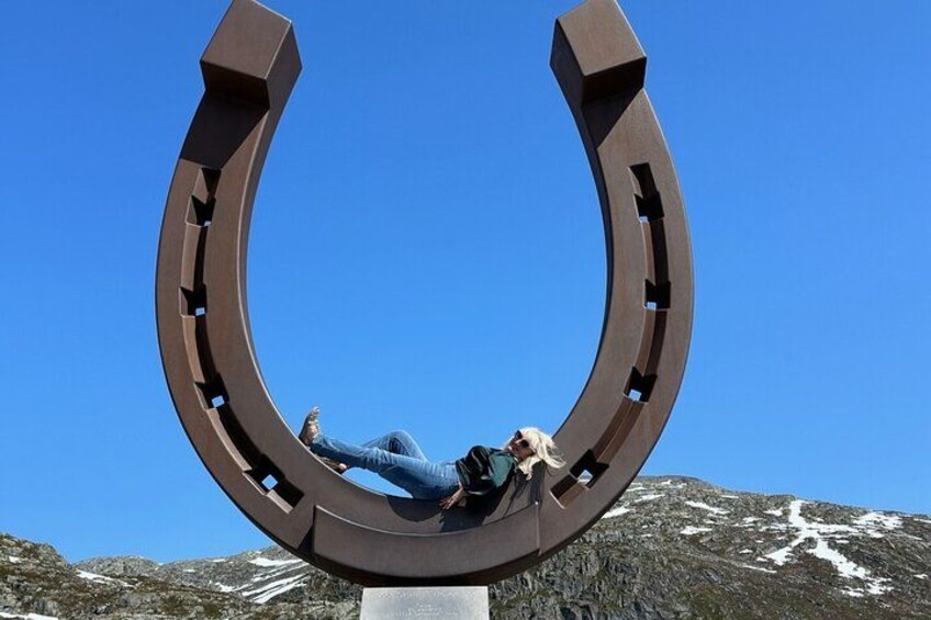 A person lying inside a large horseshoe-shaped structure with a mountainous landscape in the background. 2
