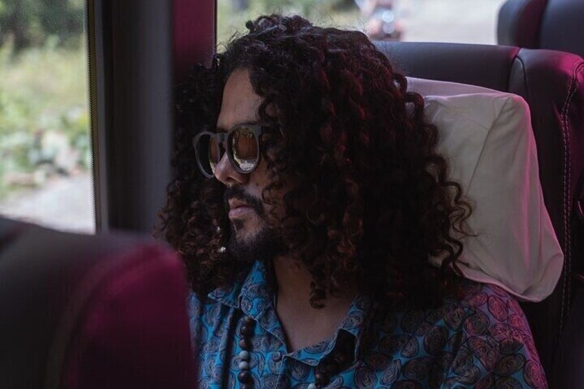A person with curly hair sitting in a vehicle with a patterned shirt. 2