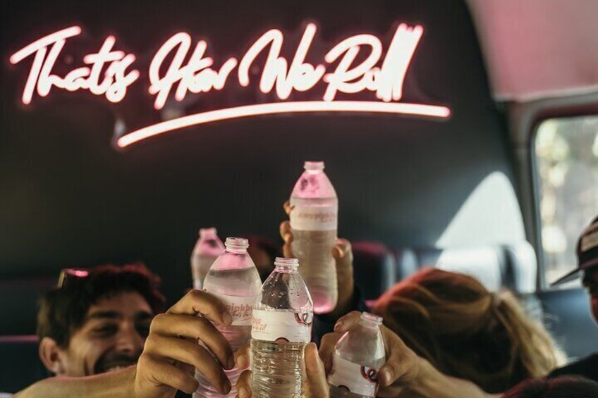 People holding bottles in a vehicle with a neon sign reading "That's How We Roll". 5