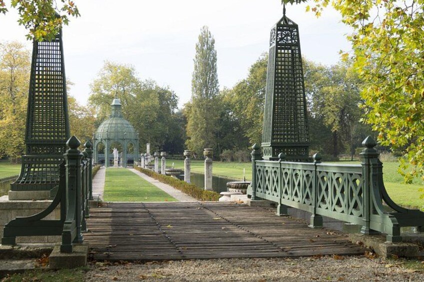 Un parc avec un pont en bois, des lampadaires en métal vert et un kiosque situé au loin. 4