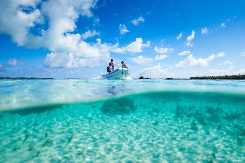 Un bateau avec deux personnes à bord, naviguant sur une mer turquoise et limpide, entouré d’un ciel bleu parsemé de nuages. 3