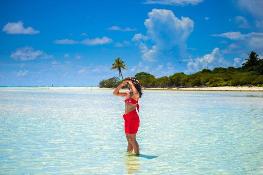 Une personne vêtue d’un maillot de bain rouge, debout dans une eau claire et peu profonde, avec une plage tropicale et des palmiers en arrière-plan. 4