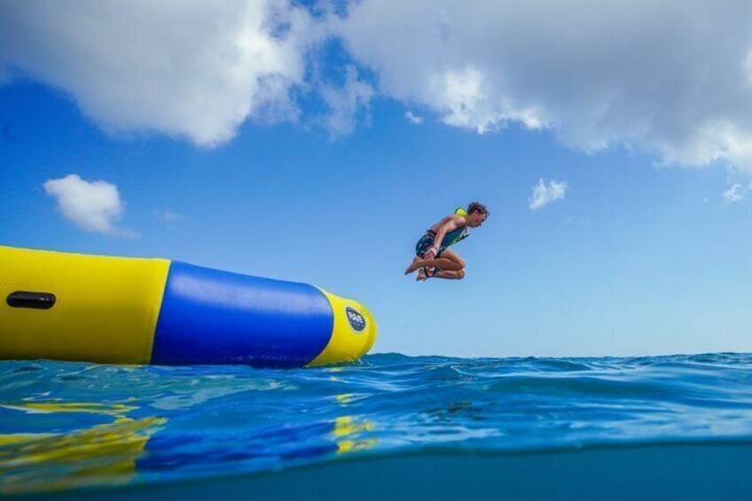 A person jumping off a yellow and blue floating platform into the ocean. 4