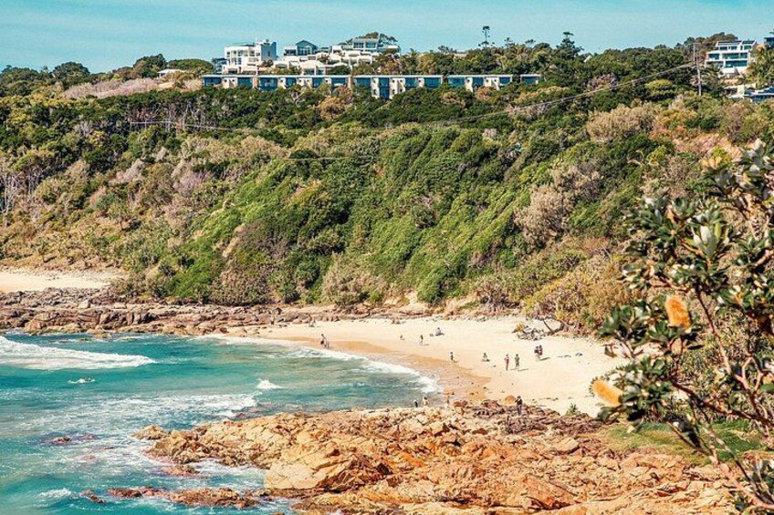 A coastal landscape with a beach, rocky shoreline, and buildings on a hill. 5
