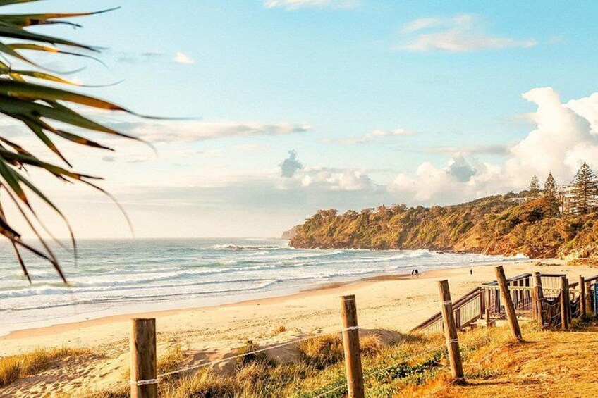 A beach with waves, a wooden fence, and a forested cliff. 2