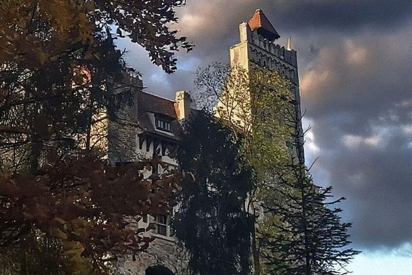 Eine Burg mit einem hohen Turm, umgeben von Bäumen und einem bewölkten Himmel. 2