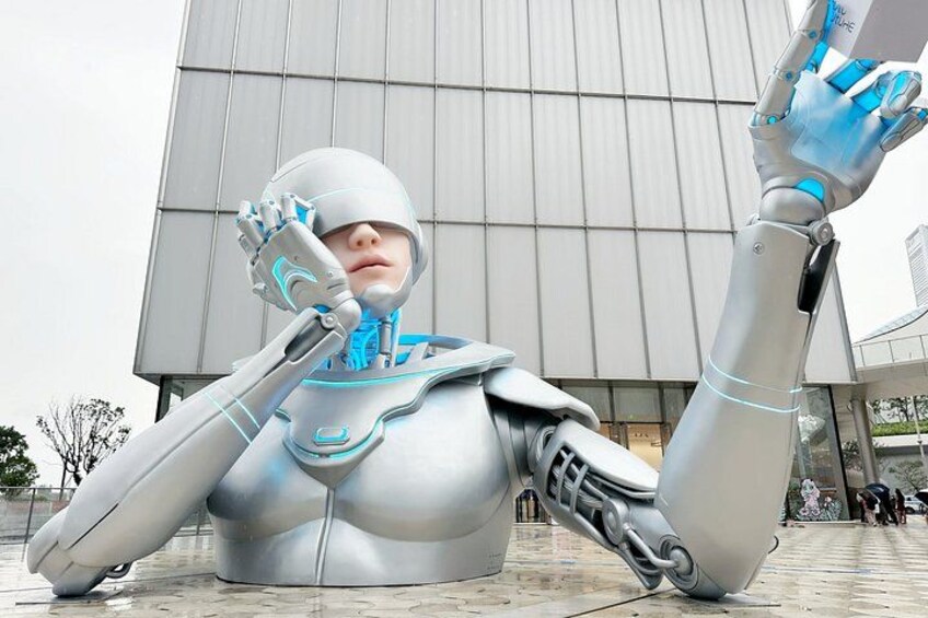 A humanoid robot sculpture in a public space with a modern building in the background. 2