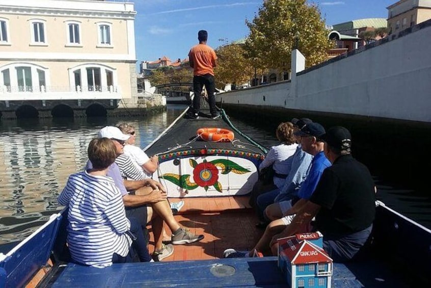 Un gruppo di persone su un'imbarcazione navigano in un canale, sullo sfondo si vedono degli edifici, e l'imbarcazione ha un design colorato. 3