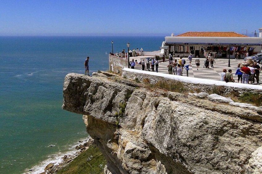 Una scogliera rocciosa con vista sul mare, un edificio con tetto in tegole e persone radunate sul promontorio. 4