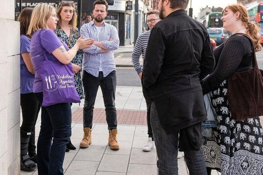 Un grupo de personas de pie en una acera, algunas vestidas con camisetas moradas con texto y otras con ropa informal. 4