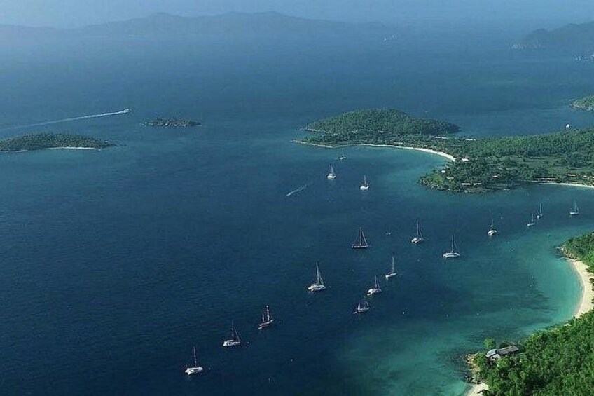 A coastal area with clear waters, several small islands, and multiple sailboats anchored near the shore. 3