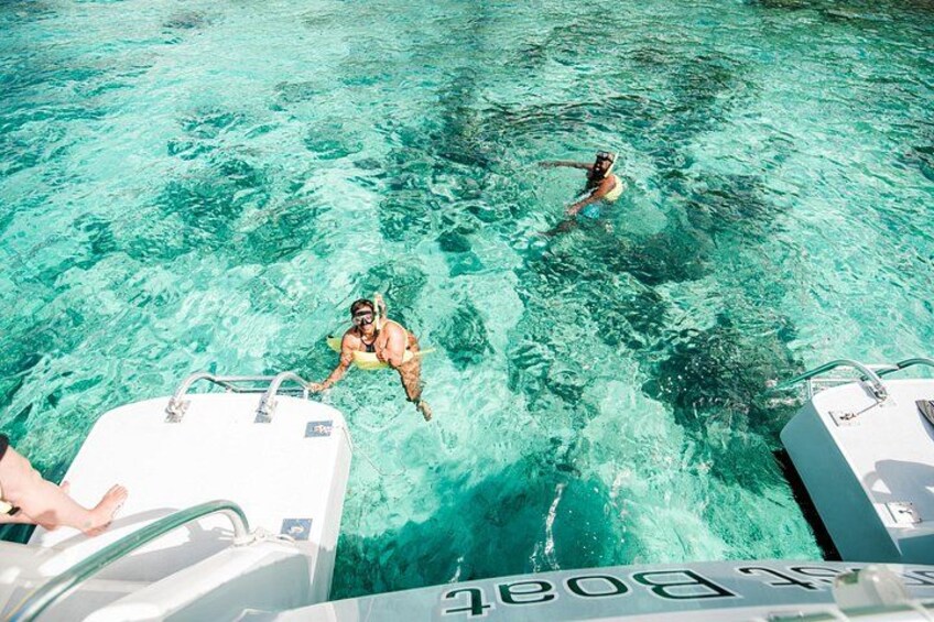 Two people swimming in clear turquoise water, with a boat in the foreground. 1
