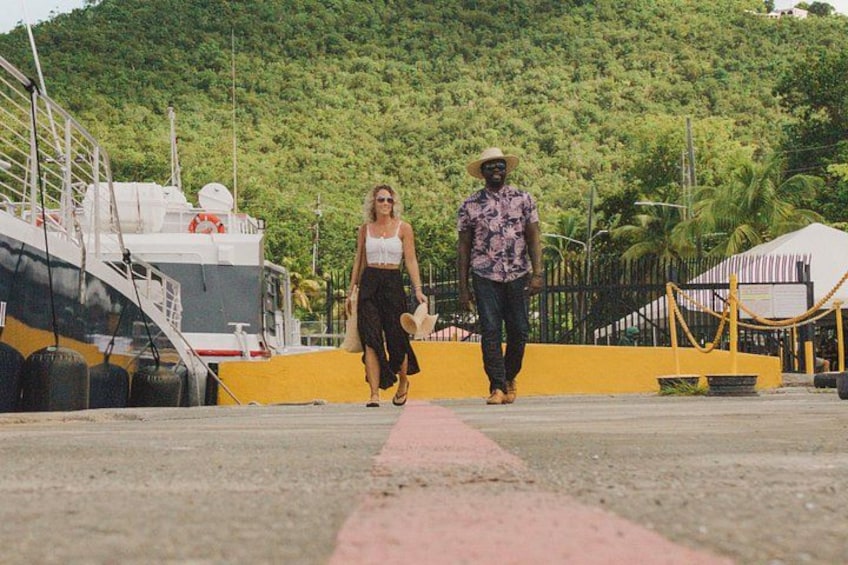 Two people walking on a dock with a boat and a mountainous background. 4