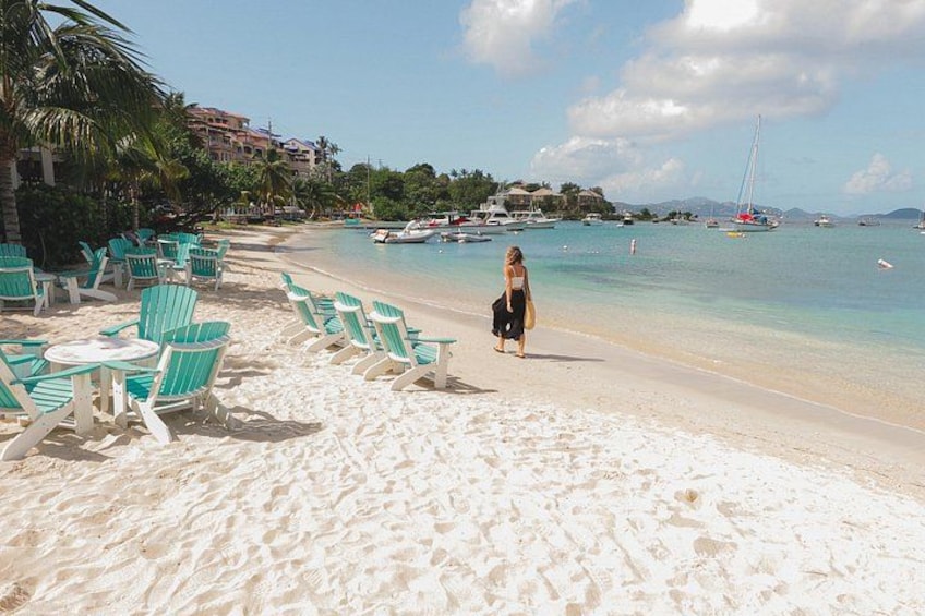 A beach with turquoise chairs, a woman walking, and boats in the water. 3