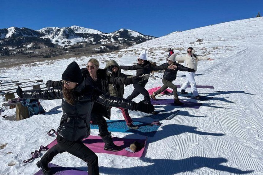 A group of people performing a snowboarding exercise on a snowy slope with mountains in the background. 3