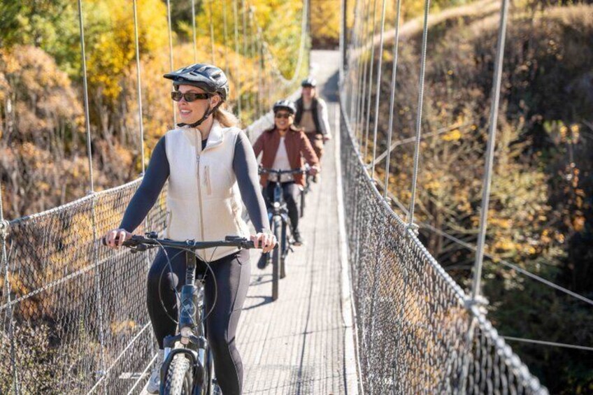 People riding bicycles on a suspension bridge surrounded by trees. 5