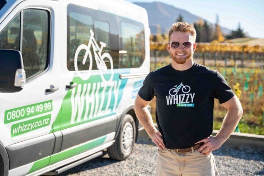 A person standing next to a white van with green and blue graphics and the text 'WHIZZY' and a bicycle symbol. 3