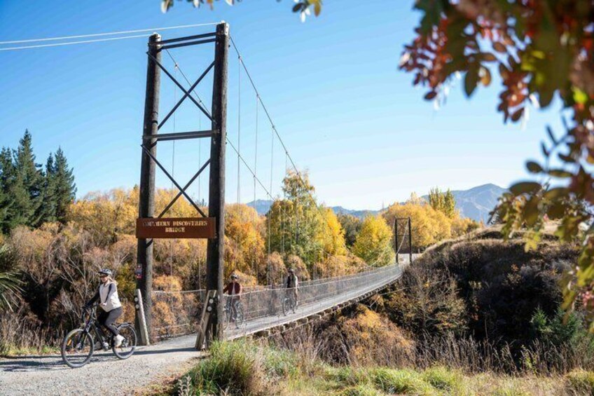 A suspension bridge with a sign, cyclists, and autumn foliage. 2