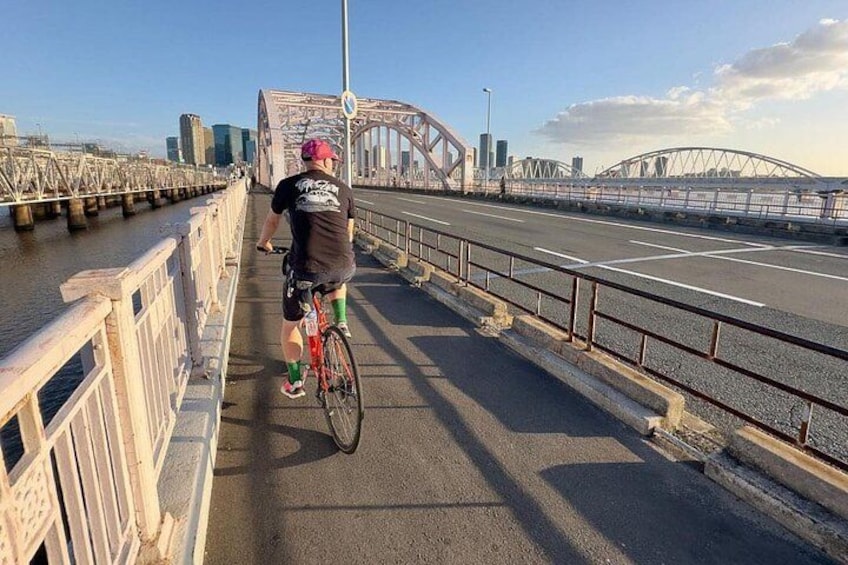 Une personne à vélo traverse un pont, avec la silhouette d’une ville en arrière-plan. 2