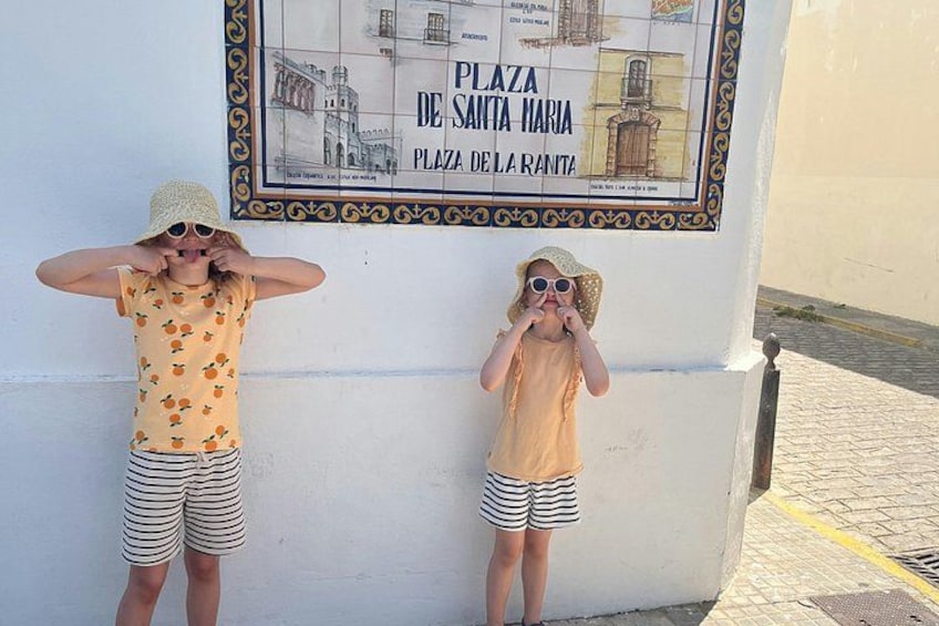 Two children standing in front of a wall with a sign that reads 'Plaza de Santa Maria.' 2