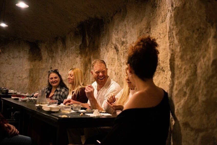 A group of people dining at a table in a rustic setting with stone walls. 1