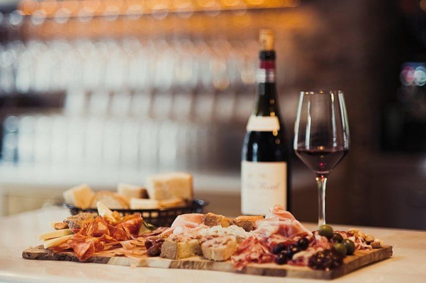 Una tabla de embutidos con diferentes carnes y quesos, una botella de vino y una copa de vino tinto sobre una mesa. 4