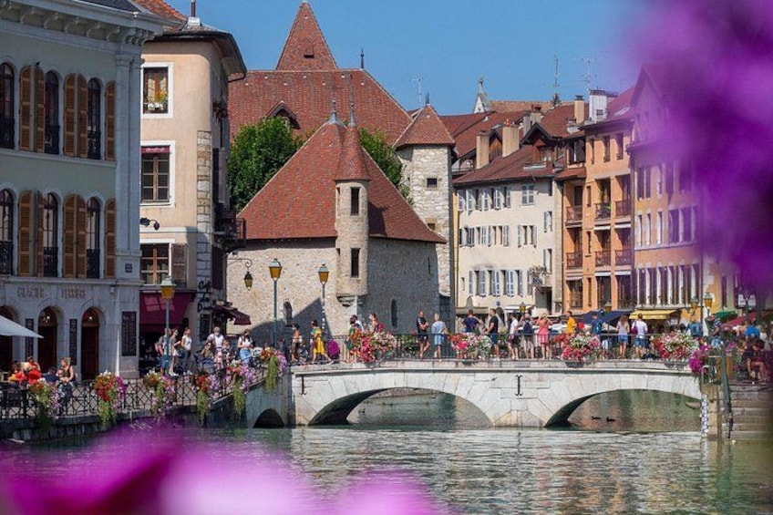 Un puente sobre el agua con gente caminando, edificios históricos y flores. 2